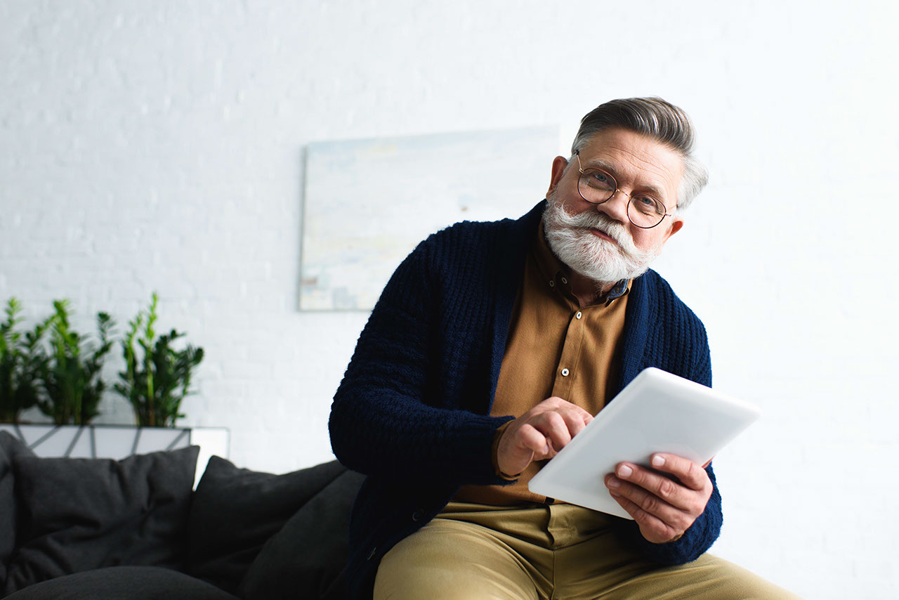 handsome bearded senior man in eyeglasses holding digital tablet and smiling at camera
