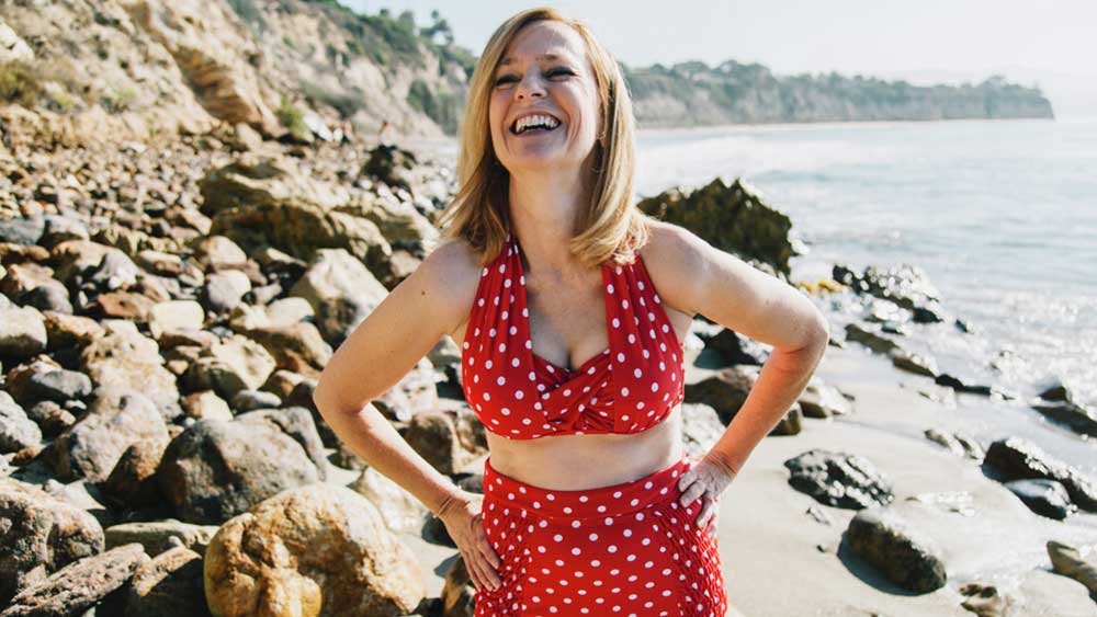 Een lachende vrouw op het strand in een rode bikini met witte stippen.
