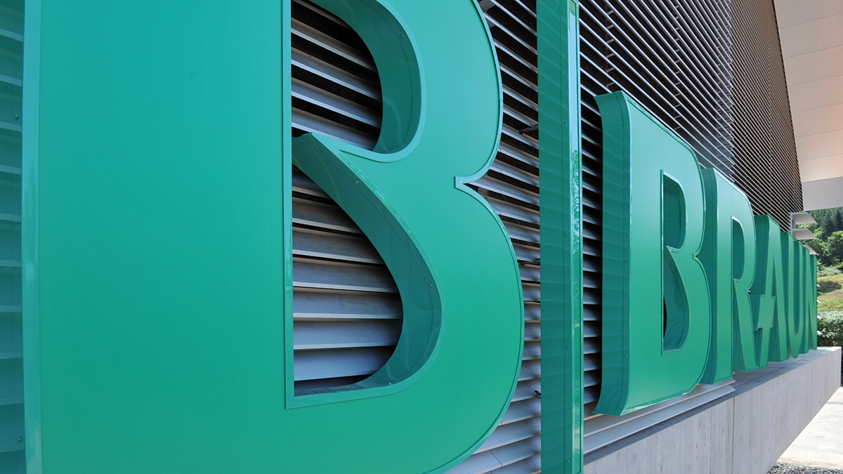 Close-up van een driedimensionaal B. Braun-logo op de gevel van een modern gebouw