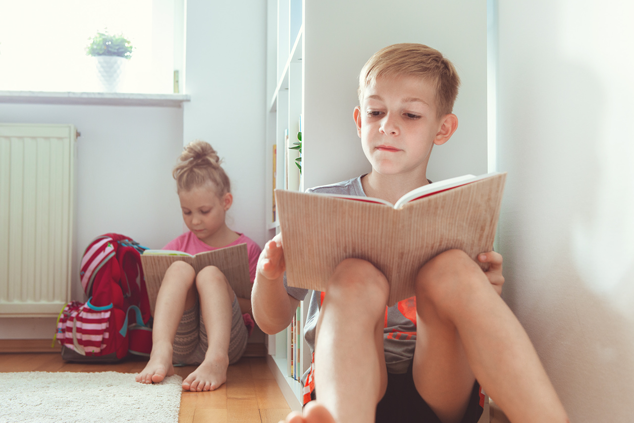 Two happy children reading books on the floor at the school  library