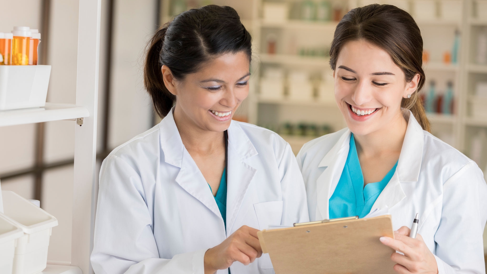 Cheerful diverse female pharmacists check on their pharmacy's inventory. They are reading something on a clipboard.