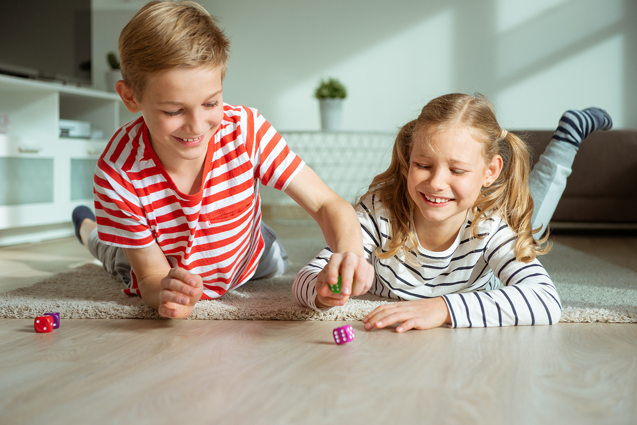 Portrait of two cheerful children laying on the floor and playing emotionally with colorful dices 