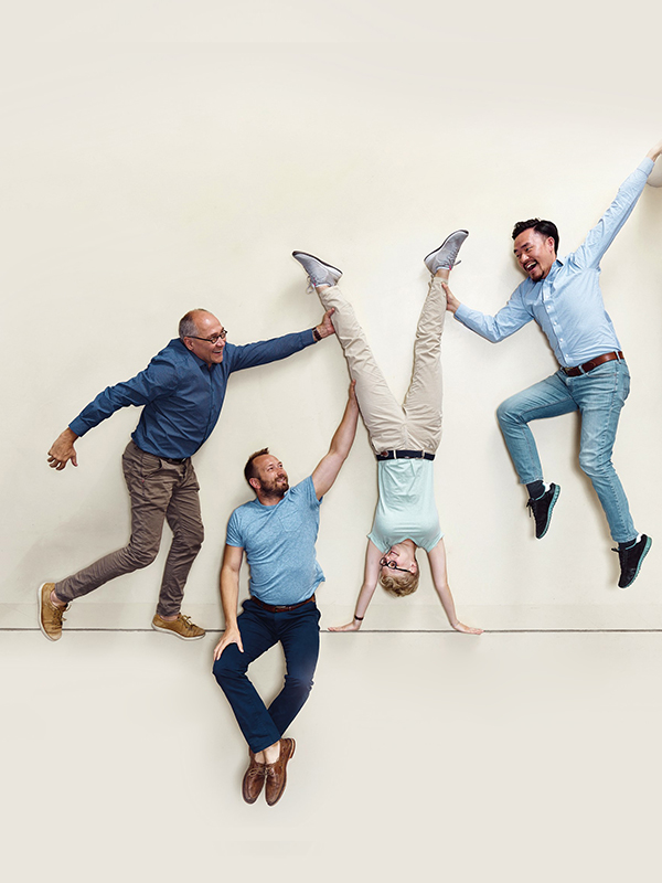 Eén persoon ondersteboven en drie andere personen houden ze vast