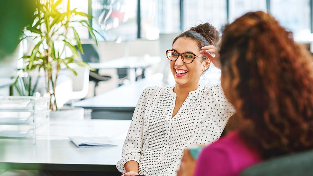 vrouw met bril opwerk lacht naar collega
