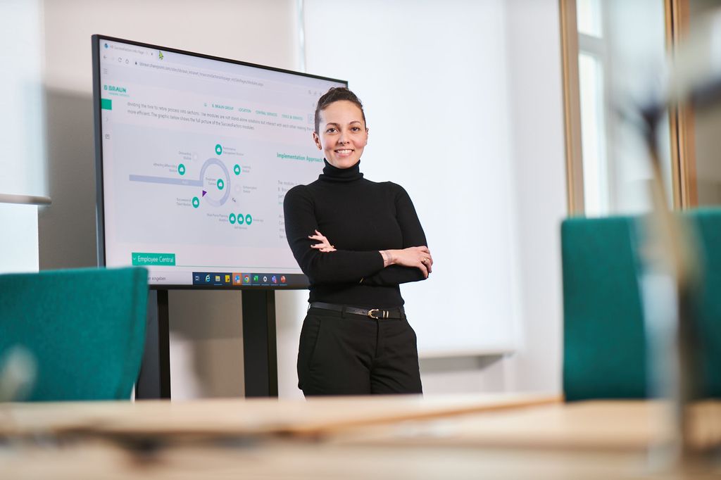 Renata Almeida, een Braun-medewerker, staat en glimlacht voor een TV die grafieken weergeeft op een kantoor. 