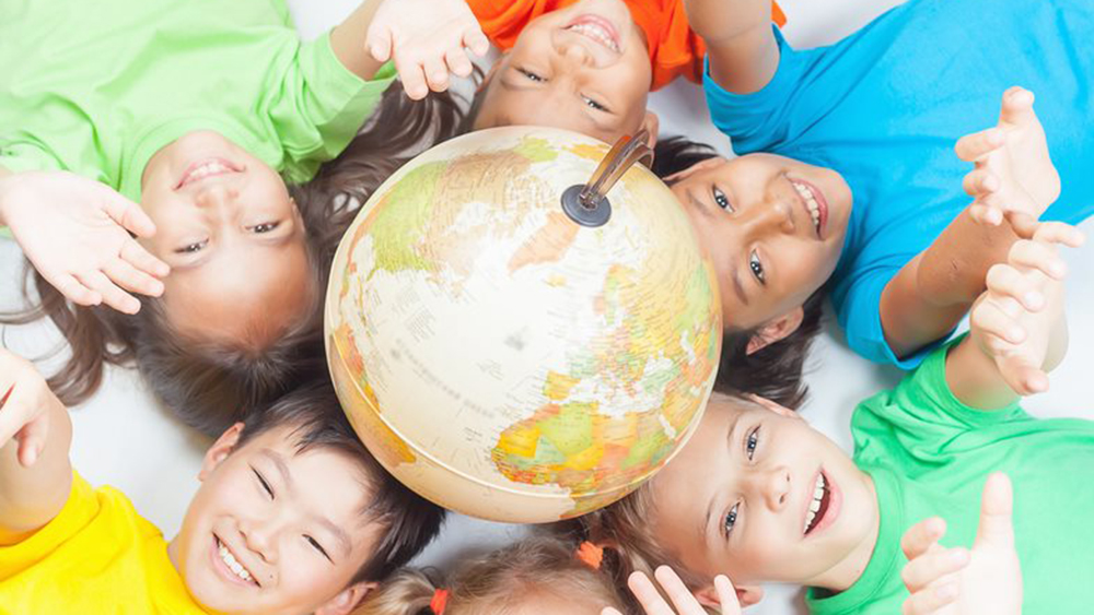 Lachende kinderen die rond een wereldbol op de grond liggen en hun armen omhoog strekken.